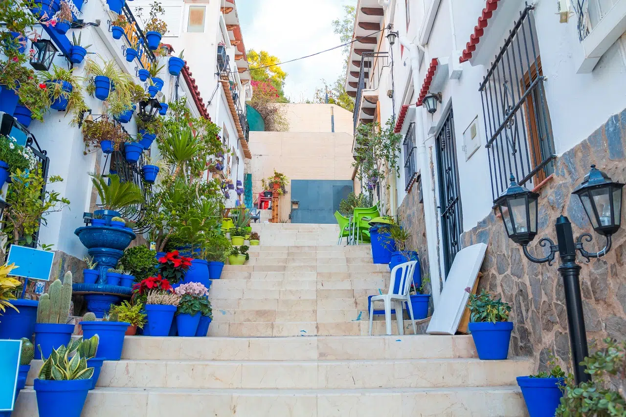 Narrow,Street,With,Steps,,White,Houses,And,Blue,Potted,Plants