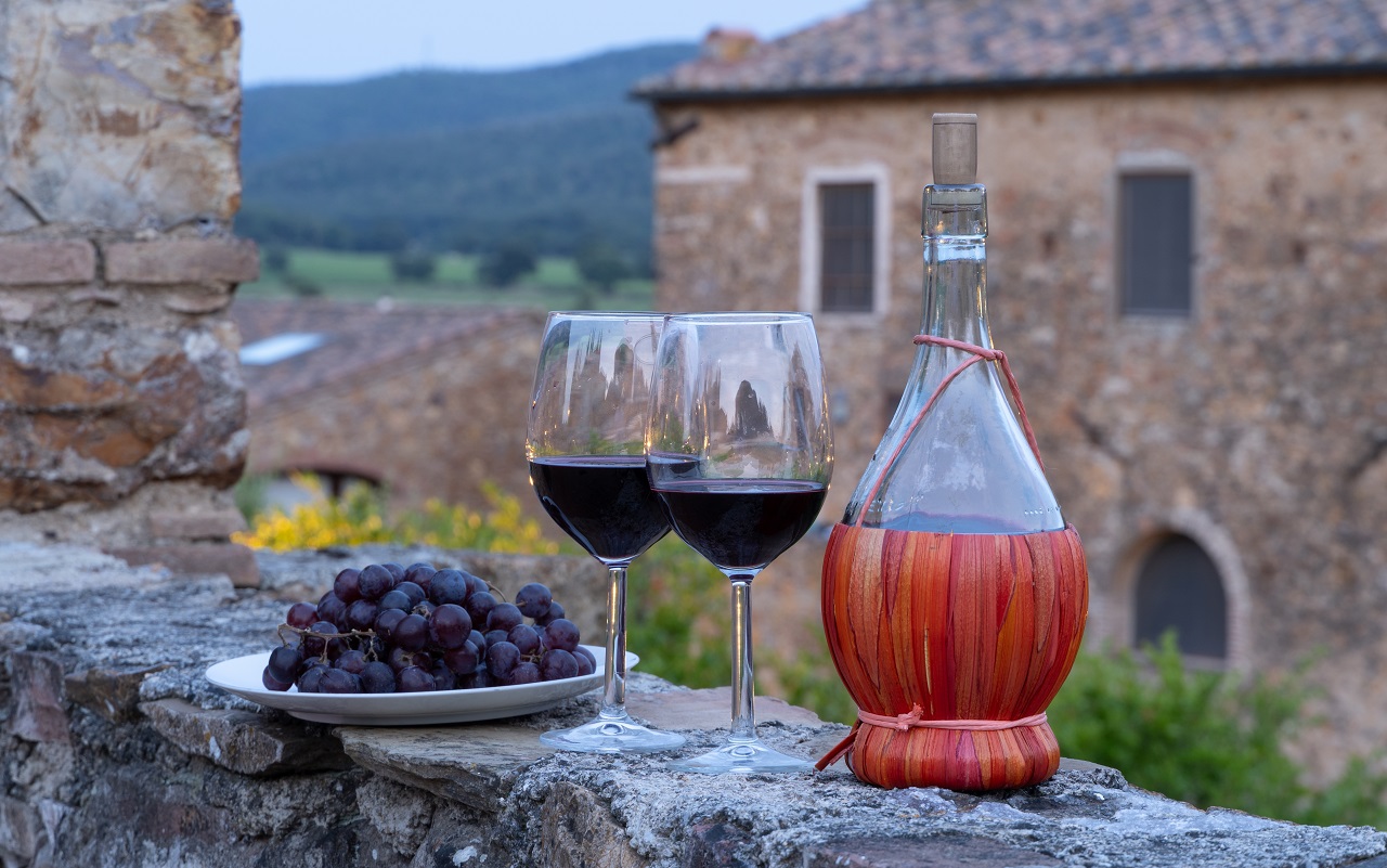 wo glasses of red wine and a Chianti bottle at a Tuscan farmhouse on a private wine tour